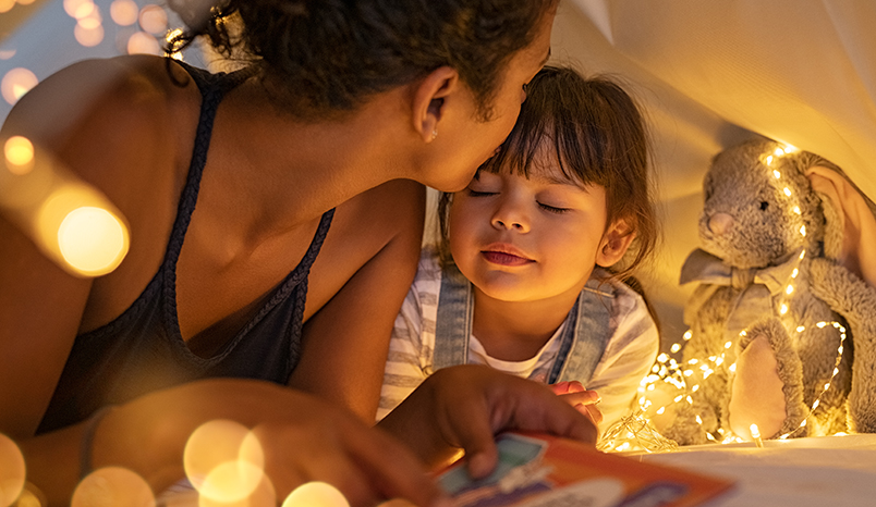 Parent kisses child on forehead before sleep.