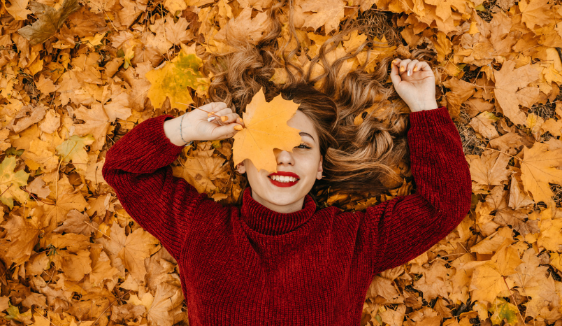 Girl in sweater smiles while laying on fall leaves.