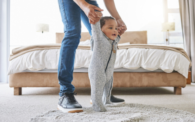 Father holds infant son's hands as he walks.