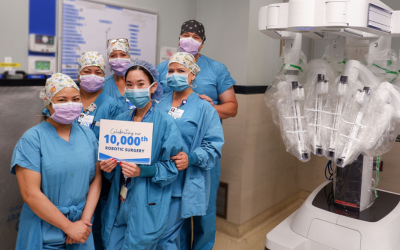 Surgical team stands next to robotic equipment.