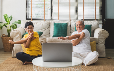 Two seniors practice seated yoga in their home.