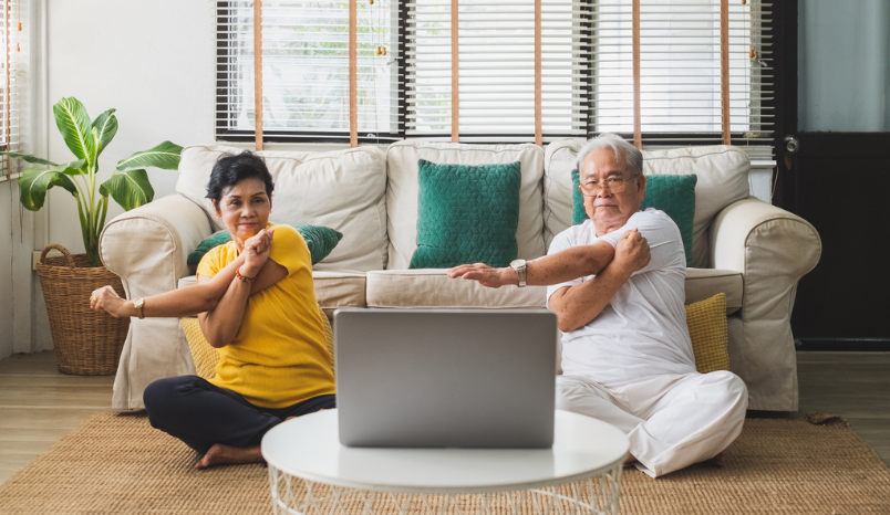 Two seniors practice seated yoga in their home.