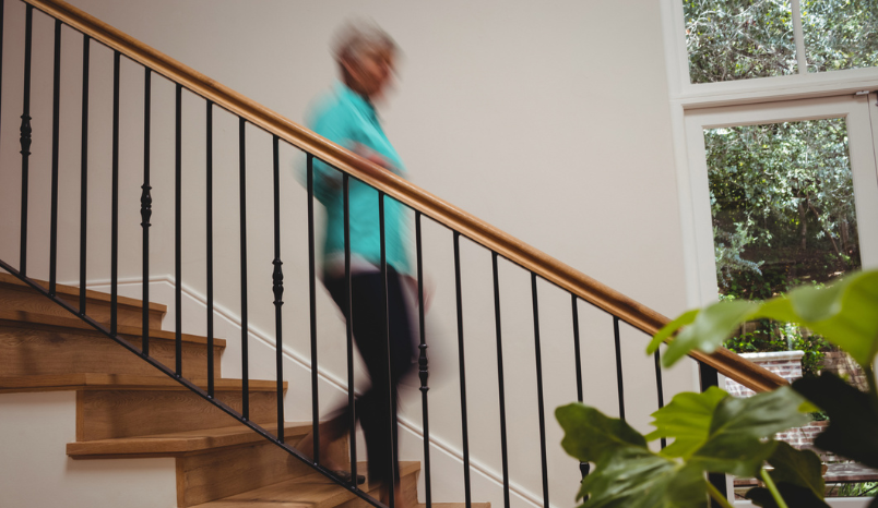 Senior woman walks down stairs in her home.