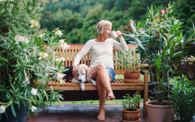 Woman sits on bench with dog while drinking out of a mug.