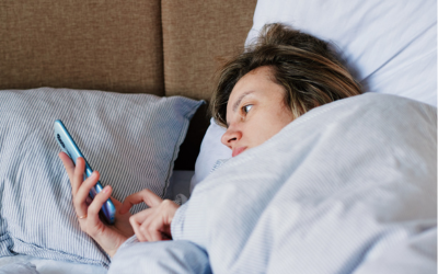 Woman laying in bed scrolls on phone.