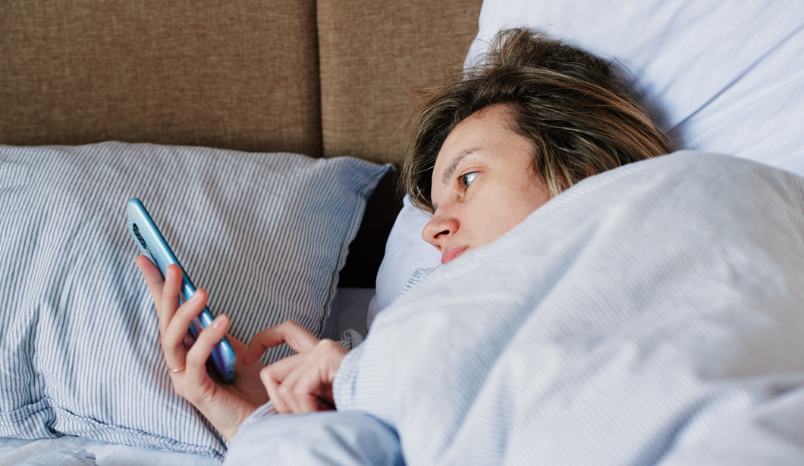 Woman laying in bed scrolls on phone.