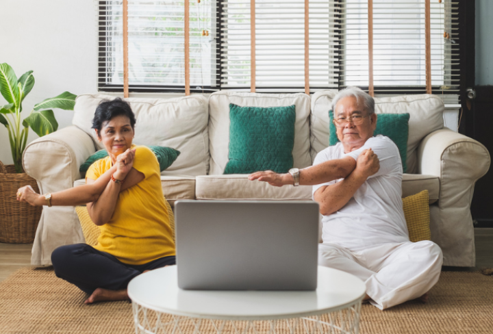 Two seniors practice seated yoga in their home.